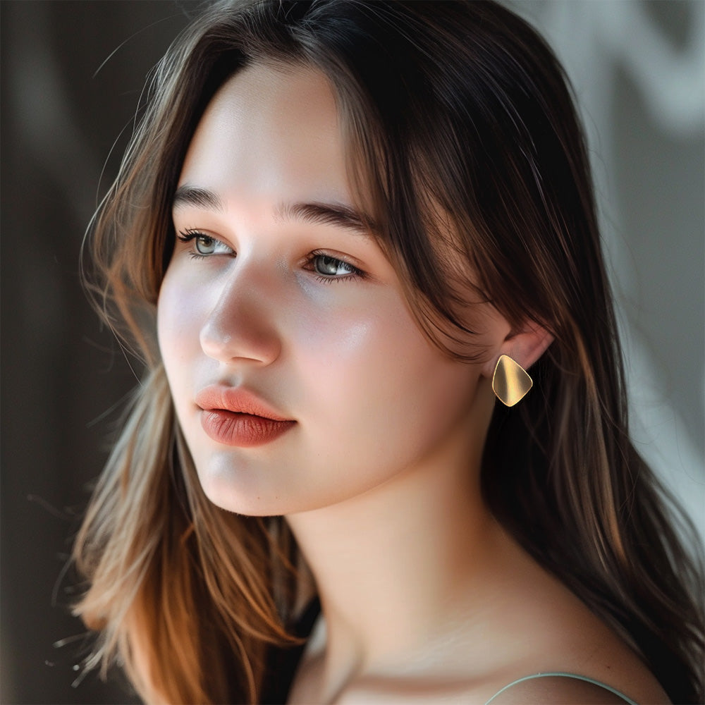 woman with golden chunky clip-on earrings with a bold geometric design. Ideal for festival fashion or everyday wear. Coil closure for comfort. Elevate your look with a touch of maximalist style.