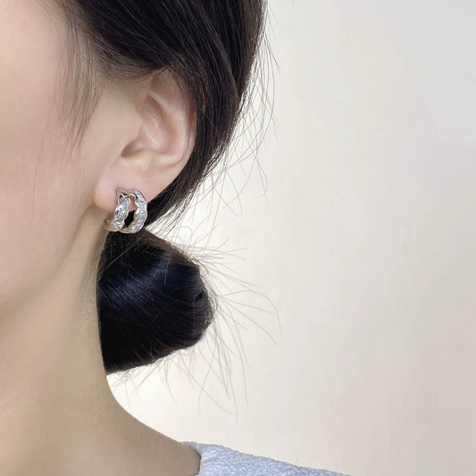 Close-up of a person wearing a white gold hoop earring with a AAA-grade cubic zirconia on a neutral background