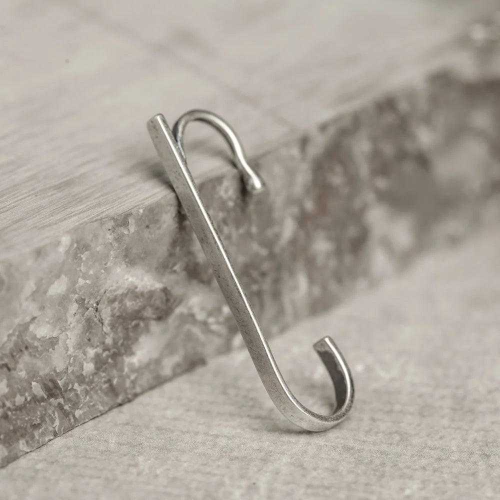 The Axis minimalist sterling silver ear cuff displayed leaning against a piece of grey stone, highlighting its shape.
