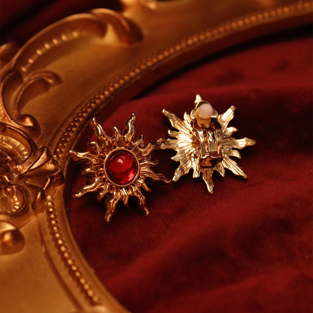 Gold sunburst clip-ons with fiery faux rubies. Hinged back for comfort. Slay your OOTD with celestial power.