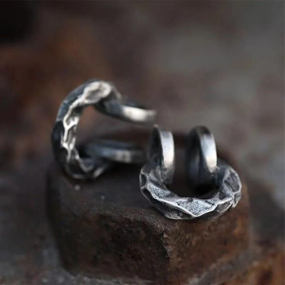 A close-up of the brutalist hammered oxidized silver clip-on ear cuff resting on a dark, rustic rock surface, highlighting its texture.