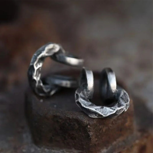 A close-up of the brutalist hammered oxidized silver clip-on ear cuff resting on a dark, rustic rock surface, highlighting its texture.