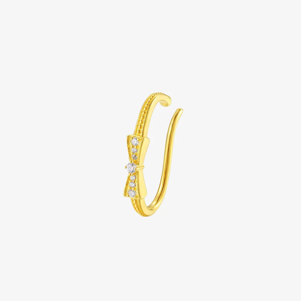 A delicate gold ear cuff featuring a pave crystal bow and milgrain band, shown on a white background.