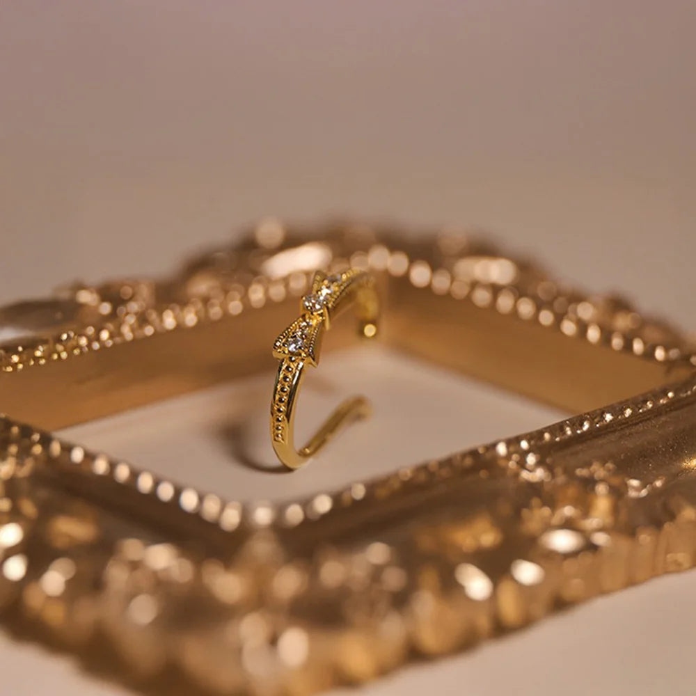 A lifestyle photo showing the delicate gold bow ear cuff resting inside a decorative gold picture frame.