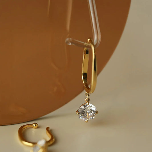 Close-up detail shot of the gold ear cuff with a dangling crystal, displayed on a clear plastic holder.