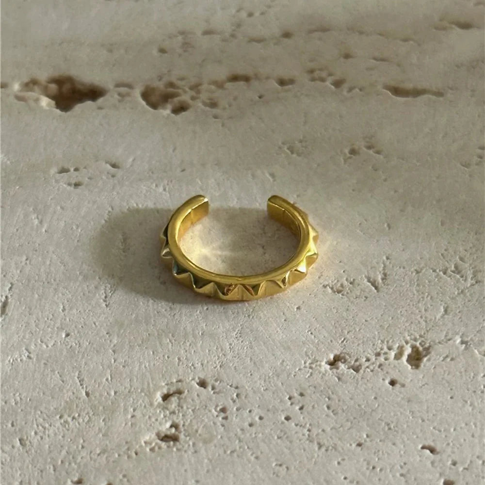 The edgy gold pyramid stud ear cuff resting on a textured beige stone surface, highlighting its polished finish.