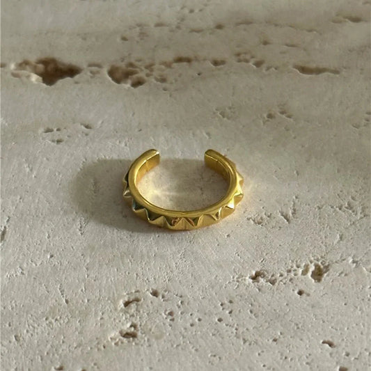 The edgy gold pyramid stud ear cuff resting on a textured beige stone surface, highlighting its polished finish.