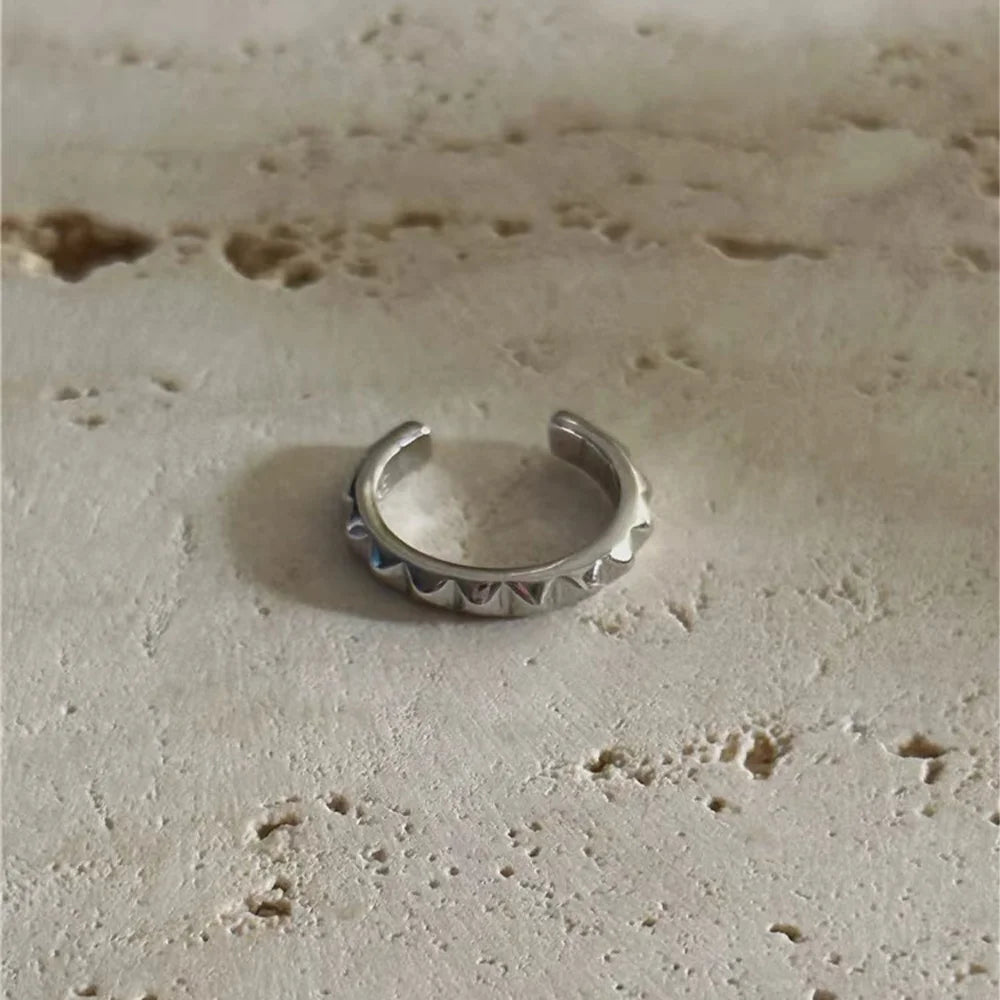 The edgy silver pyramid stud cartilage cuff resting on a textured stone surface, showcasing its polished and rebellious design.