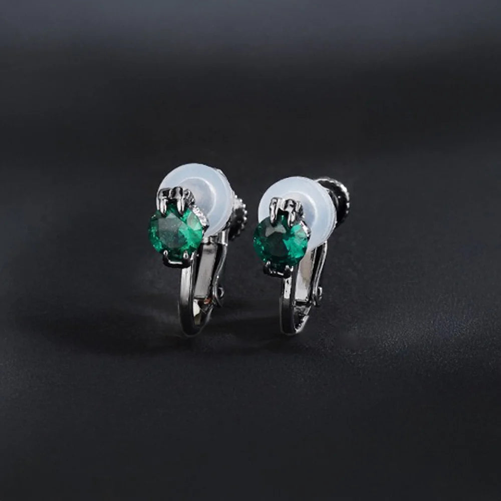 A pair of elegant emerald green cubic zirconia clip-on stud earrings in a silver-tone setting with comfortable cushioned clip-on backs.