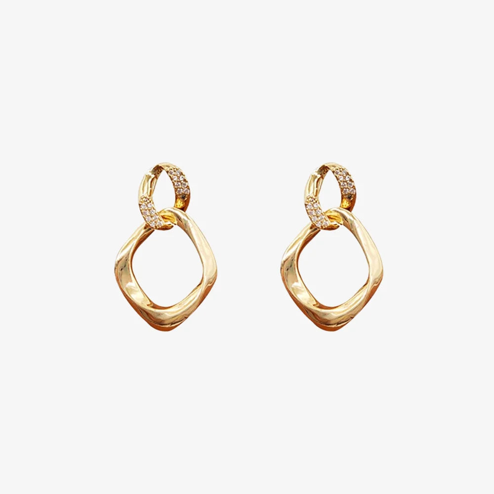 Pair of gold geometric pave drop earrings on a light gray background