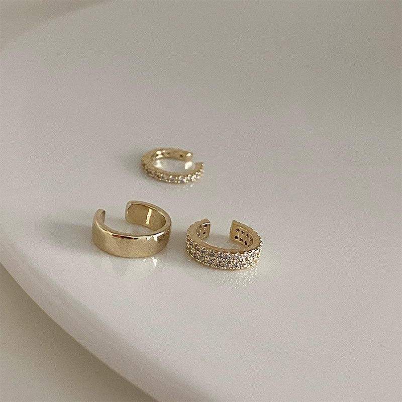 An artful display of the trio of gold and pavé zirconia ear cuffs on a neutral, curved white surface.