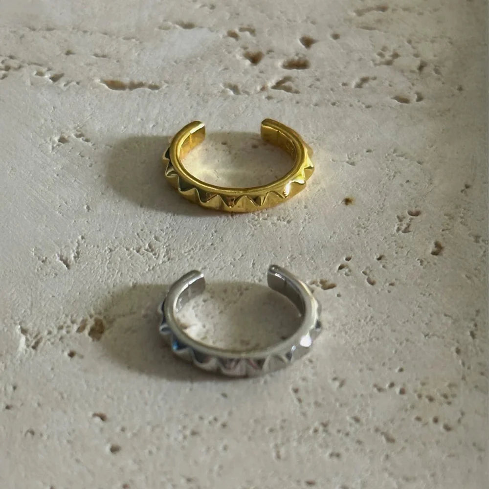 Both the gold and silver studded sterling silver cartilage cuffs shown together on a stone surface to compare finishes.