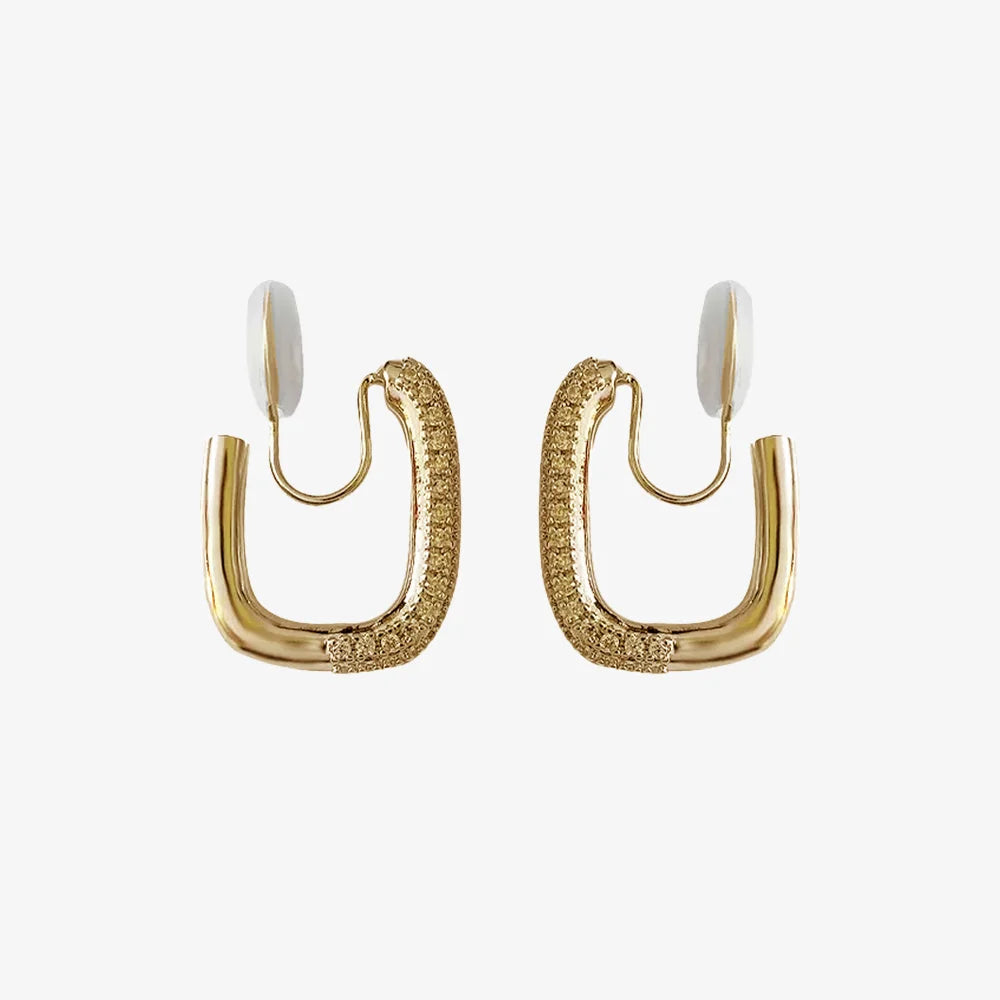 A pair of gold pavé square clip-on hoop earrings with white comfort pads, shown on a white background.