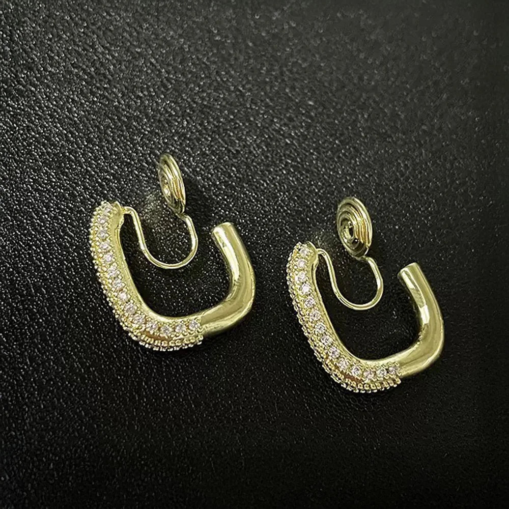 A detailed view of the gold pavé square clip-on hoop earrings on a black surface, showing the sparkling cubic zirconia and the adjustable clip-on mechanism.