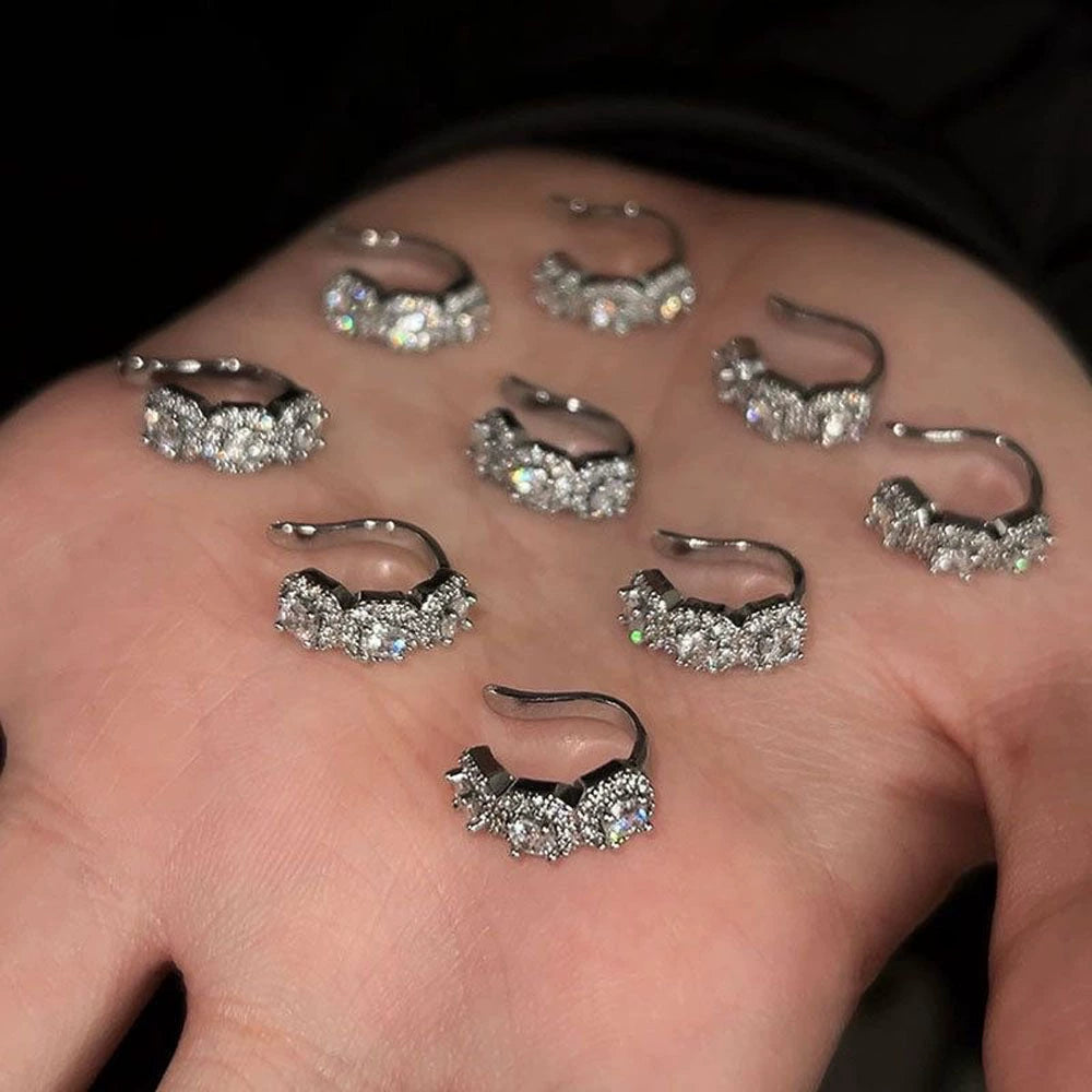 A collection of Halo Nova silver triple zircon pavé clip-on ear cuffs displayed on an open hand, showcasing their brilliant sparkle and design.