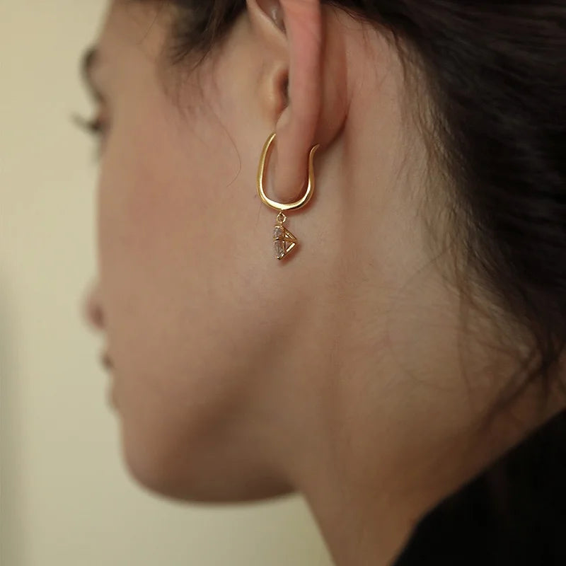 A view from behind of a model wearing the gold solitaire dangle ear cuff, showing how it hugs the cartilage of the ear.