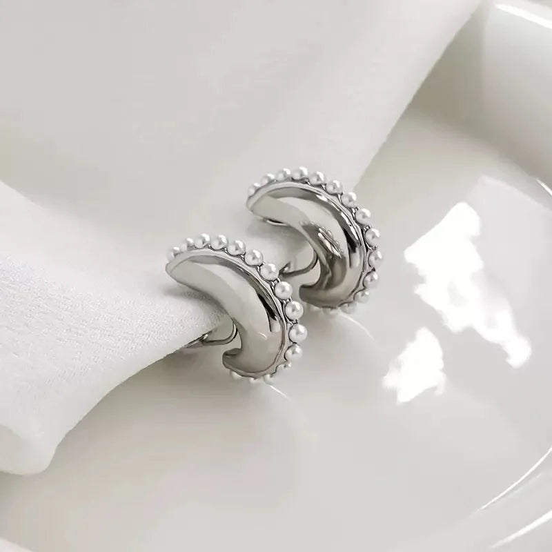 A lifestyle shot of the Luna pearl crescent clip-on earrings resting on a white napkin and plate, highlighting their polished finish.