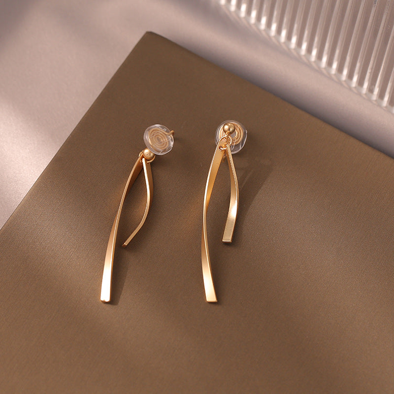 Dangle clip-on earrings feature a slender ribbon design for a touch of modern elegance. Made from gold-tone copper alloy with a secure coil clip closure, they're perfect for those with non-pierced ears.  Elevate your everyday look with these versatile earrings.