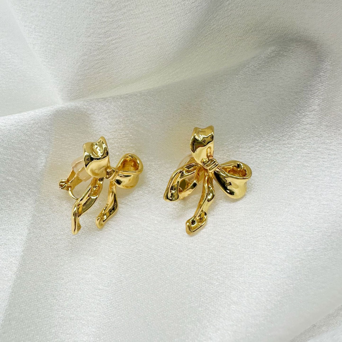 Gold bow clip-on stud earrings for a touch of whimsical charm. Hinge back closure for comfort. The perfect finishing touch for your spring style outfit.