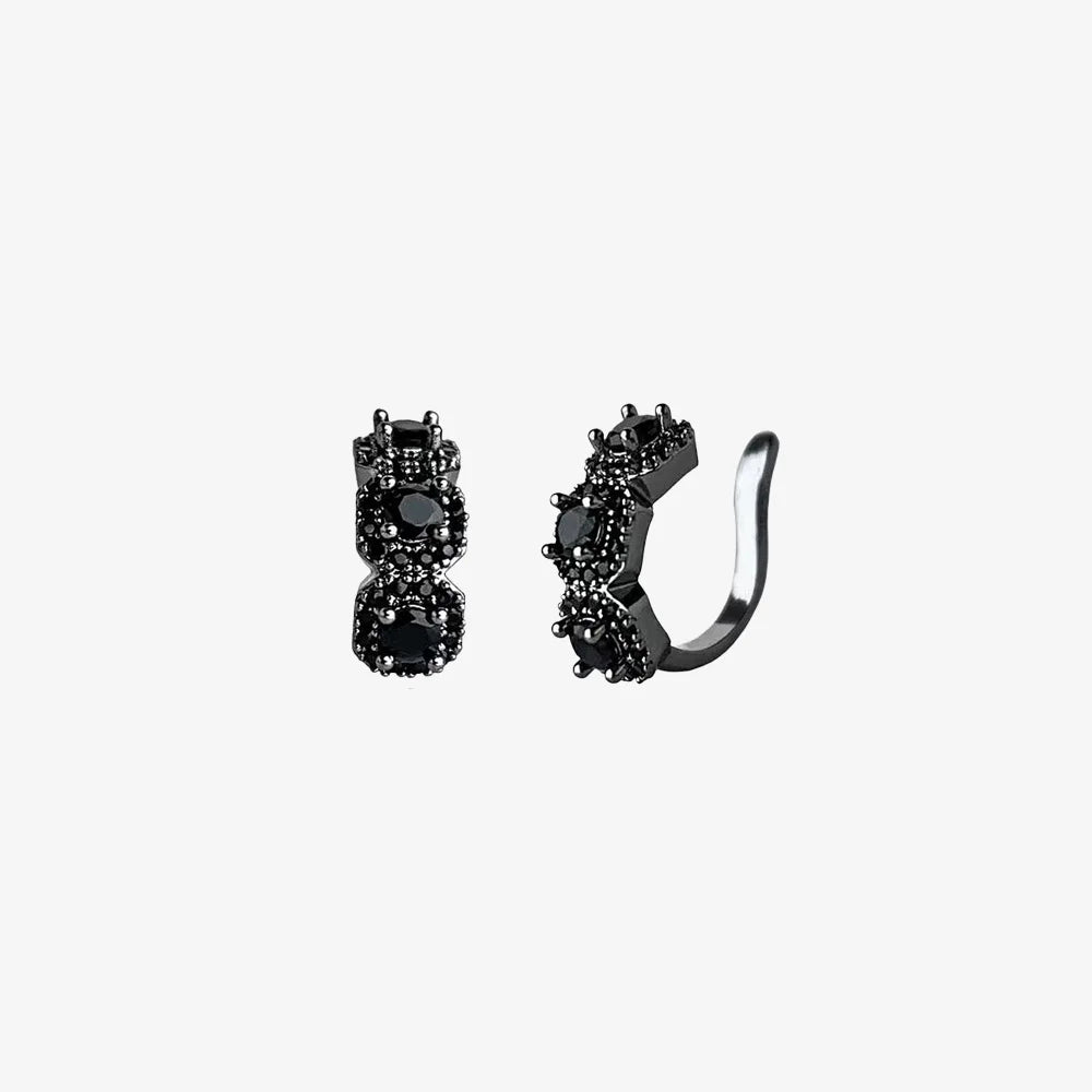 A studio shot of a pair of Midnight Star black triple zircon pavé clip-on ear cuffs on a clean white background, highlighting their dark sparkle and intricate details.
