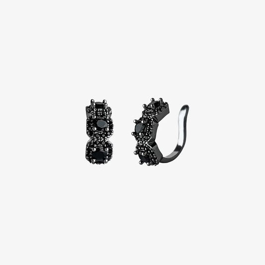 A studio shot of a pair of Midnight Star black triple zircon pavé clip-on ear cuffs on a clean white background, highlighting their dark sparkle and intricate details.
