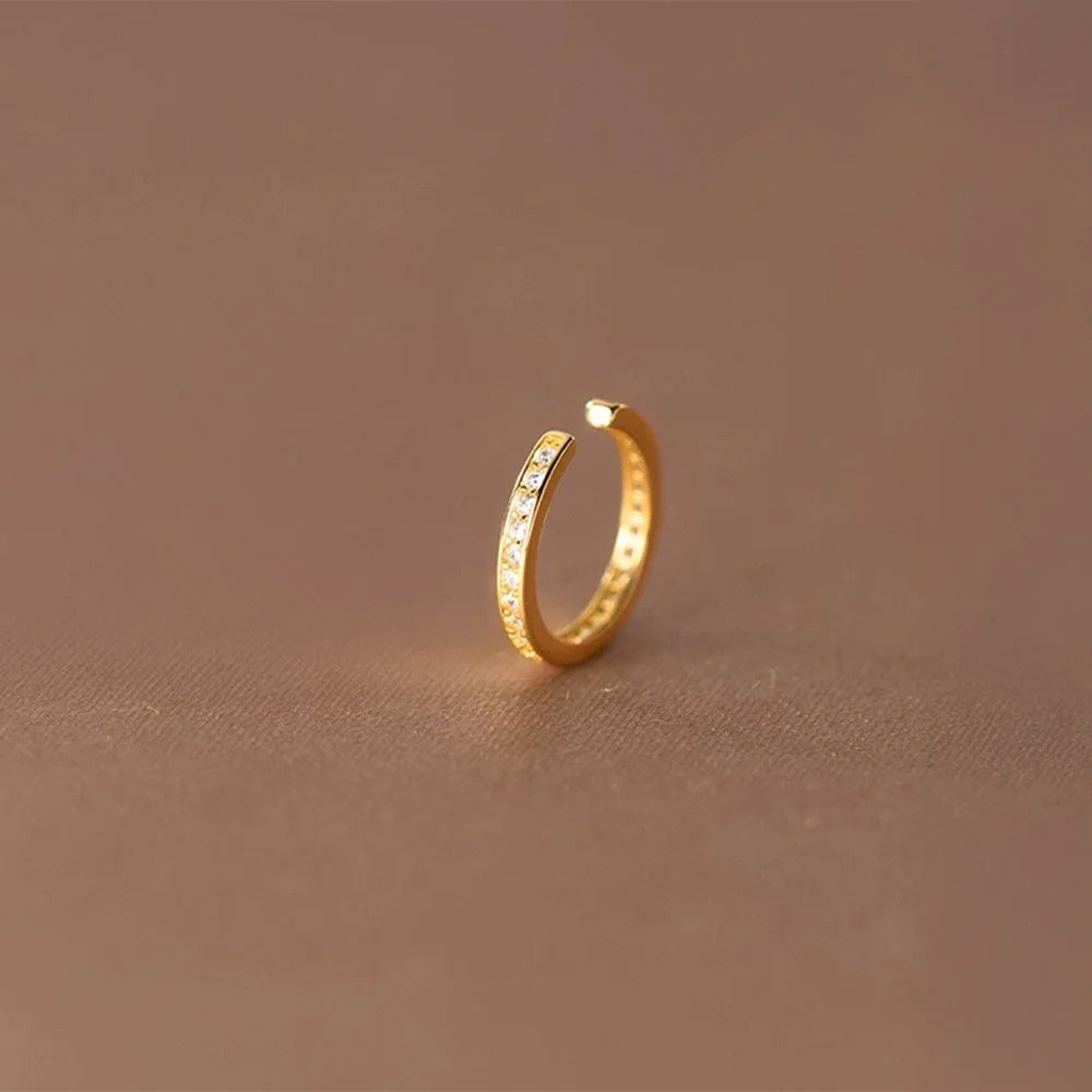 Close-up of the minimalist pavé gold ear cuff, showing the sparkling cubic zirconia stones on a neutral brown background.