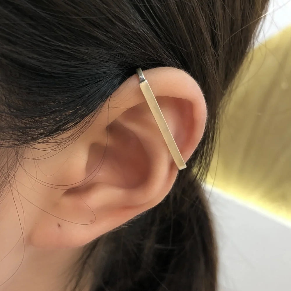 Close-up shot of a model's ear wearing the Axis sterling silver minimalist wrap ear cuff, which wraps vertically along the helix.