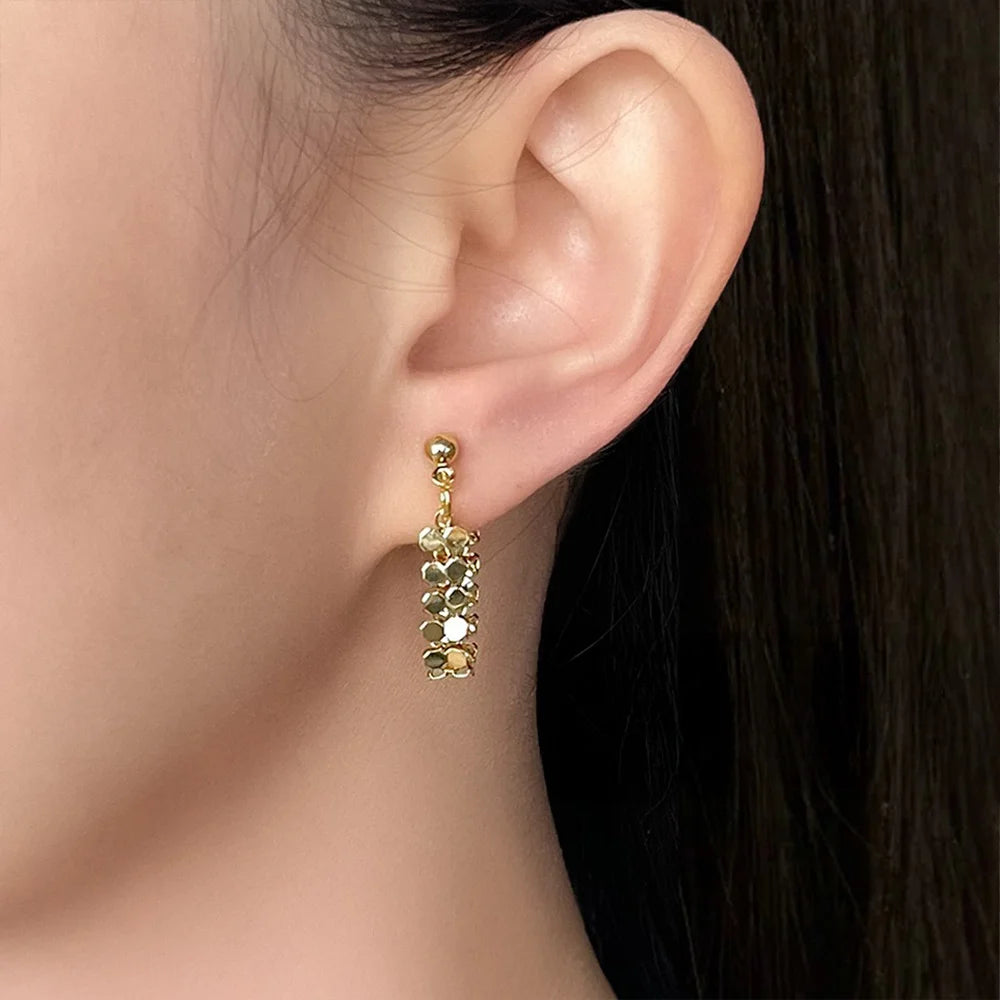 Close-up of a model wearing the gold hexagon mesh dangle clip-on earring to display its size and elegant drop.