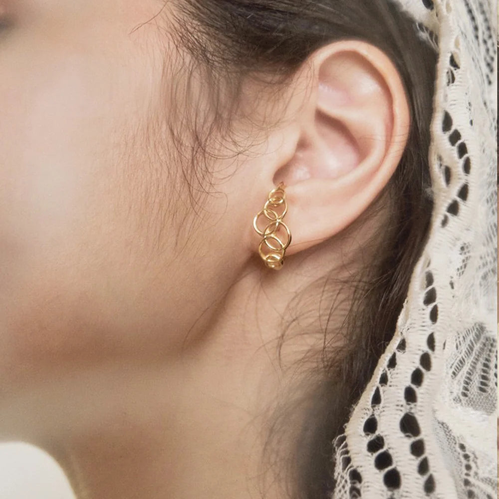 A model wearing the gold interlocking circle ear cuff on her earlobe, showing the faux hoop effect.