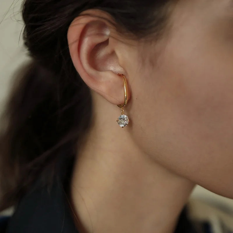 A model's ear shown from the front, wearing the gold ear cuff with a dangling crystal on her lobe.