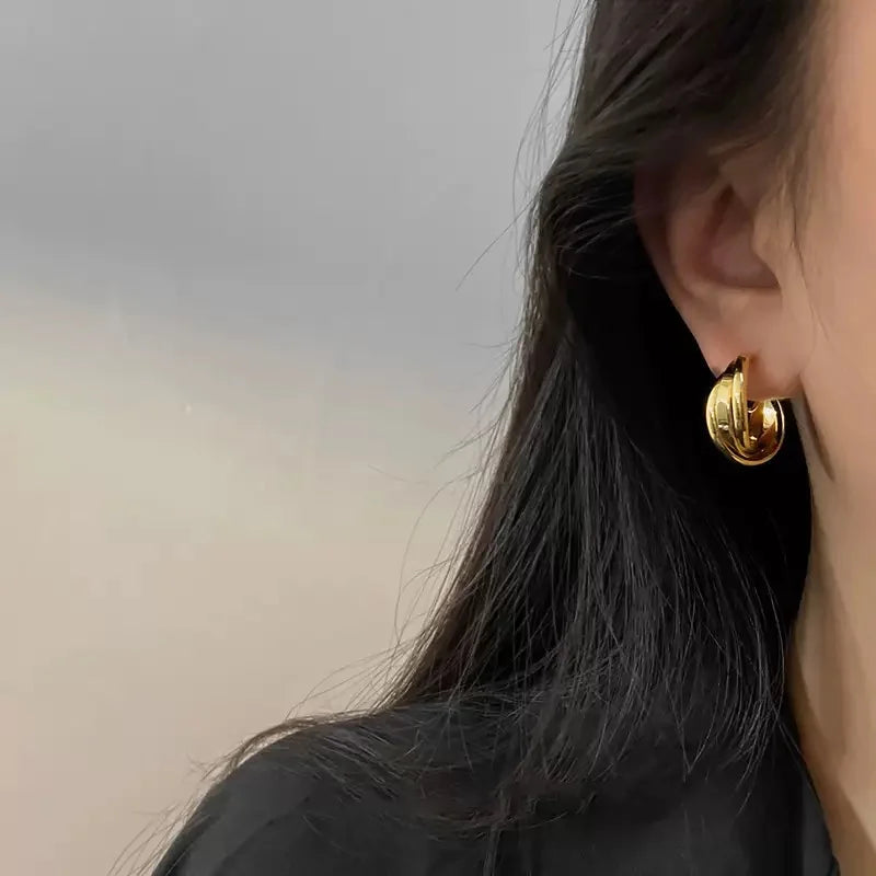 A model wearing the gold layered wave clip-on huggie hoops, showing their size and stylish look on a non-pierced ear.