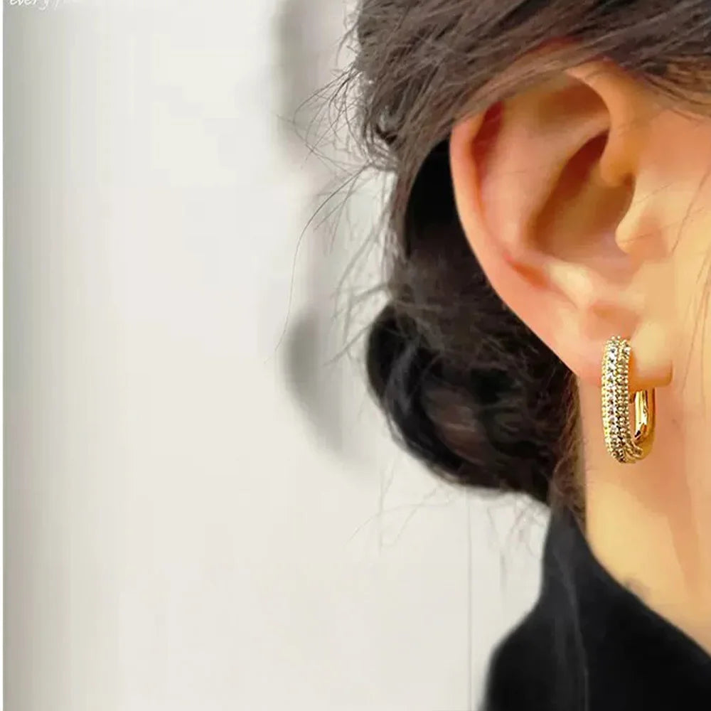 A close-up of a model's ear wearing the gold pavé square clip-on hoop earring to showcase its size and how it looks when worn.