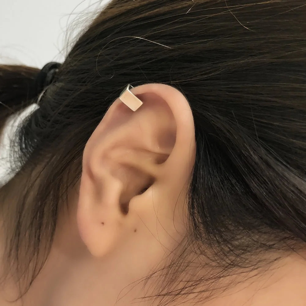 A close-up of a model's ear wearing the small sterling silver bar ear cuff on the upper helix cartilage for a subtle, modern look.