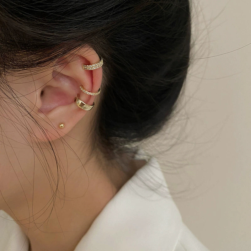 A model showcasing a curated ear look with the complete stacked set of three gold ear cuffs on her cartilage and helix.