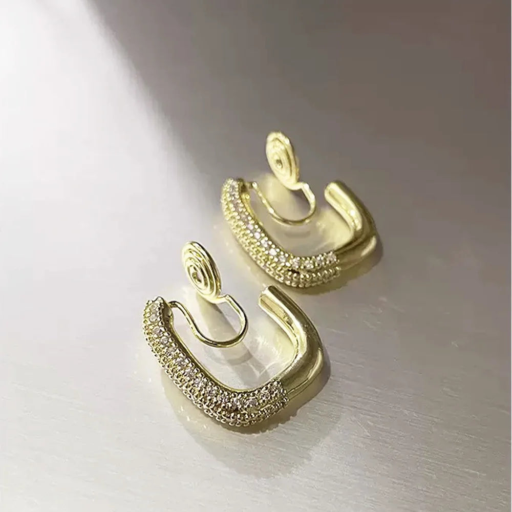 Angled product shot of the gold U-shaped clip-on pavé earrings on a bright, reflective surface, highlighting the sparkling cubic zirconia stones.