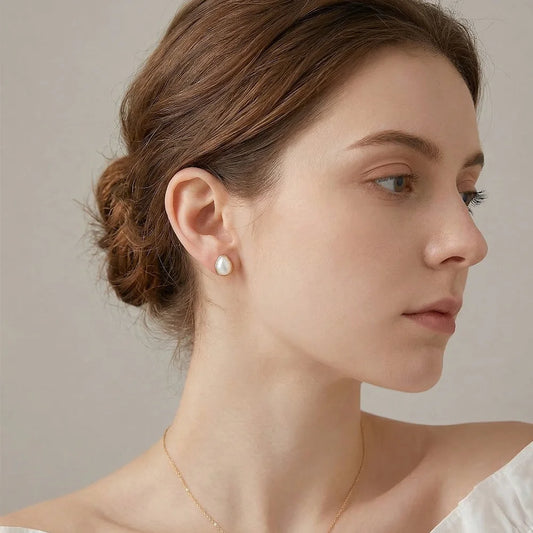 Profile view of a woman wearing a single teardrop mother of pearl clip-on earring in rose gold, paired with an elegant updo and white top.