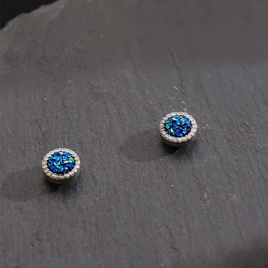 A pair of Nova Iridescent Blue Galaxy Magnetic Stud Earrings, showcasing their sparkling blue druzy texture on a dark slate background.