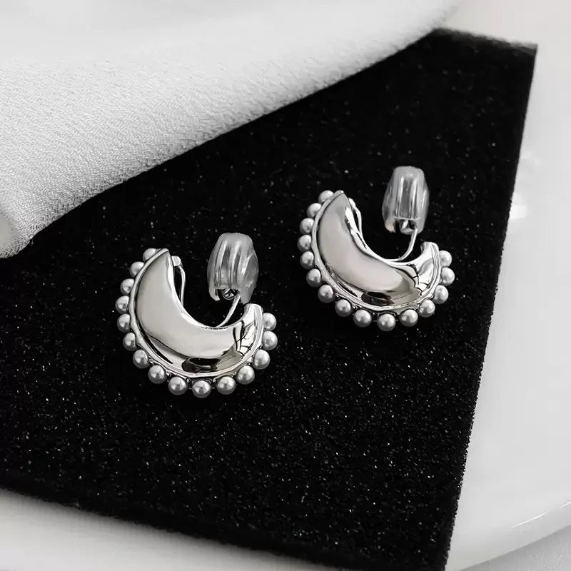 A pair of Luna pearl crescent clip-on earrings displayed on a black textured surface next to a white cloth.