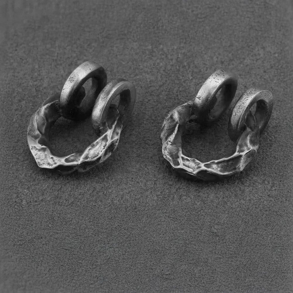 A pair of hammered oxidized silver clip-on cartilage cuffs, showcasing their rugged texture on a dark grey background.