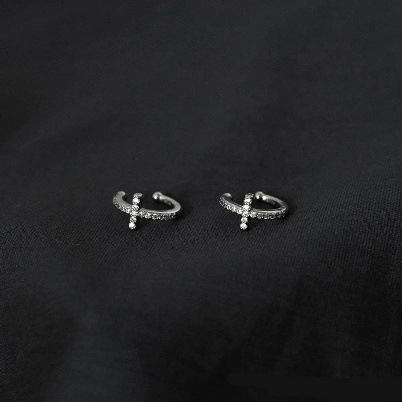 A pair of pavé silver cross clip-on cartilage cuffs, showcasing their sparkling details on a dark background.