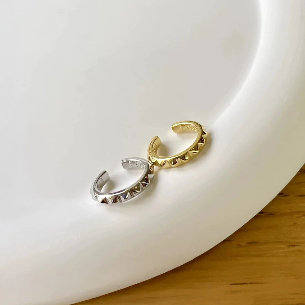 The gold and silver studded ear cuffs displayed together on a curved white dish, showcasing their punk-inspired design.