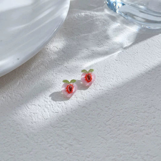 Two sweet peach magnetic clip-on earrings resting on a white textured surface under soft sunlight, showing the translucent jelly-like resin texture.