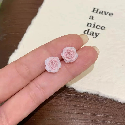 A pair of pink rose magnetic stud earrings held delicately in a hand, highlighting their intricate petals and small size.