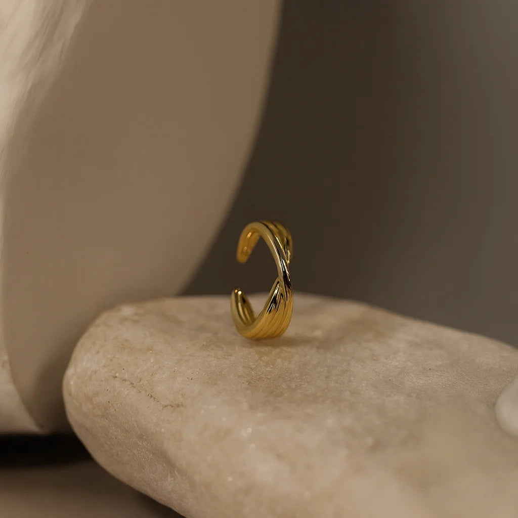 Side profile of the wide, twisted gold ear cuff resting vertically on a stone, highlighting its C-shape opening.