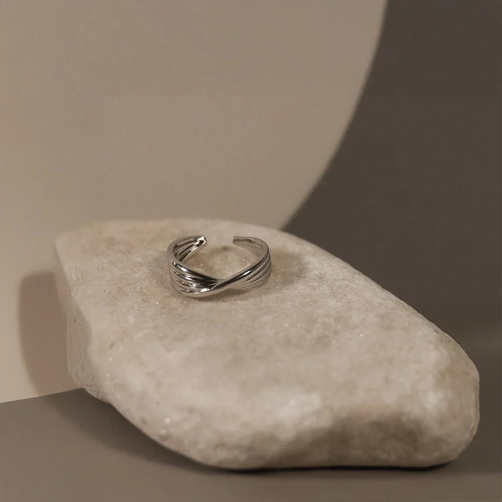 A side profile of the wide, twisted silver ear cuff resting on a stone, highlighting its C-shape opening for the ear.