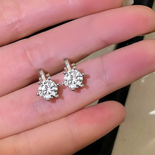 A close-up of the pair of silver cubic zirconia clip-on stud earrings being held in a hand to show their size and sparkle.
