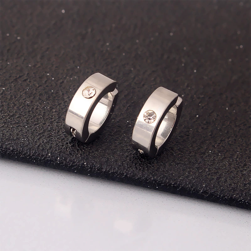 A pair of silver minimalist clip-on huggie hoops with a single zircon stone, displayed on a white surface against a dark background.