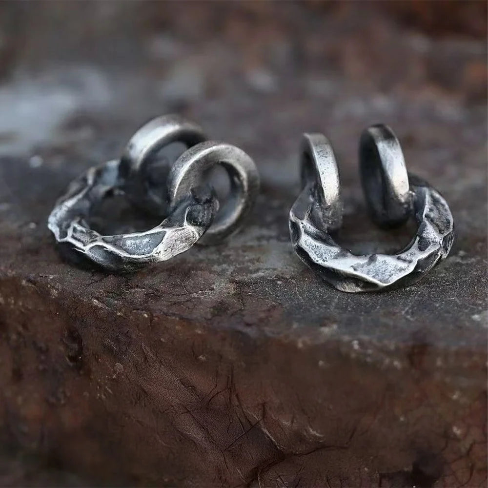 Two hammered oxidized silver ear cuffs displayed on a metallic surface, emphasizing their raw, industrial-inspired texture.