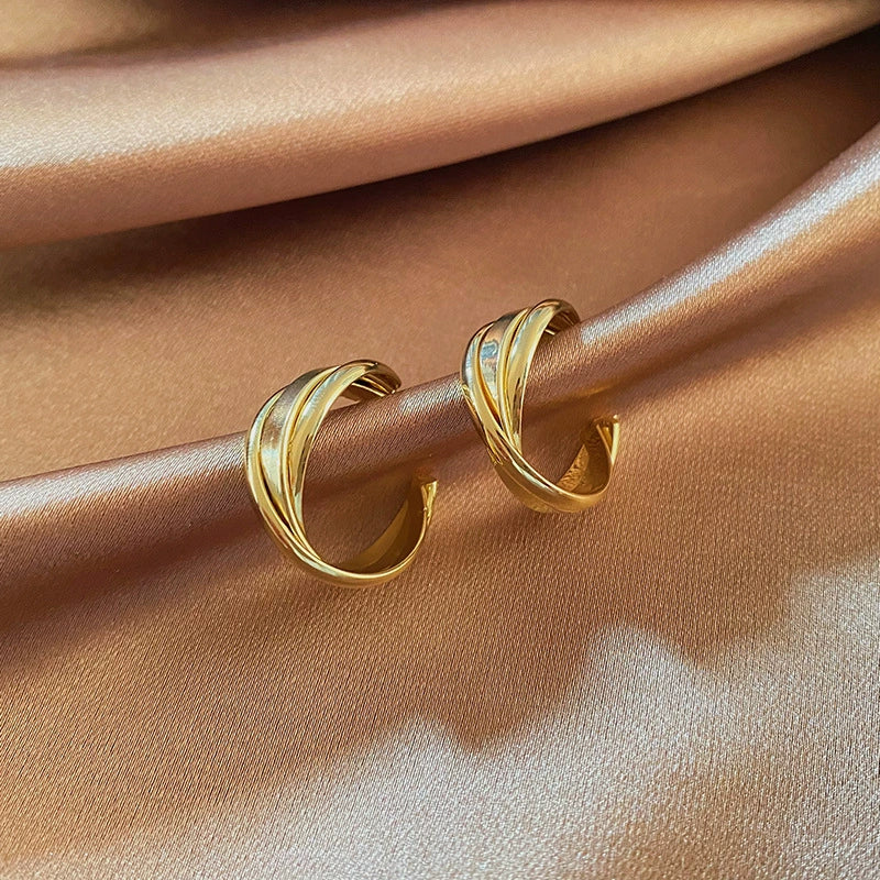 A side view of the twisted gold C-hoop clip-on earrings, showcasing their sculpted layers and polished finish on a satin surface.