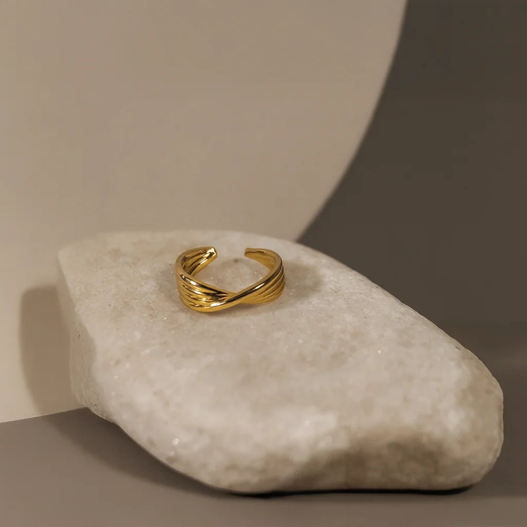 Gold crossover ear cuff displayed on a natural white stone, showing its warm tone and layered texture.